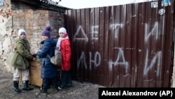 Дети стоят возле забора поврежденного дома с надписью «Дети и люди» в оккупированном Мариуполе, 25 февраля 2023 года. Украинские хакеры KibOrg получили доступ к базе данных «Дети Донбасса»