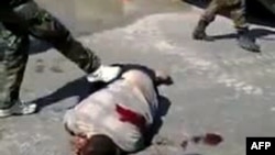 A Youtube video grab shows what antiregime activists in Syria say are pro-government militia members dressed as soldiers kicking the corpse of a man in the city of Homs on September 5.