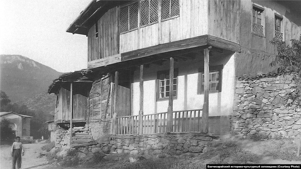 Сельский дом. Юго-Западный Крым, 1920-ые. Стандартный интерьер главной комнаты включал открытый камин с дымоходом и подвешенный к нему на цепи казан. Вдоль стен стояли низкие диванчики с матрацами и подушками, рядом &ndash; столики. Для украшения стен использовались многочисленные полотенца, а для пола &ndash; ковры